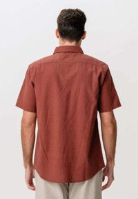 Kortærmet skjorte i rustfarve med button-down krave, glat tekstur og rygstykke, vist fra bagsiden.