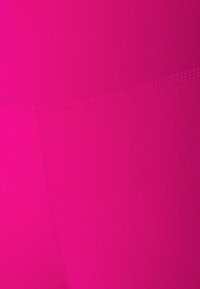 Lähikuva kirkkaan vaaleanpunaisesta kankaasta, jossa näkyvät saumat, ja joka näyttää sileältä ja eloisalta.