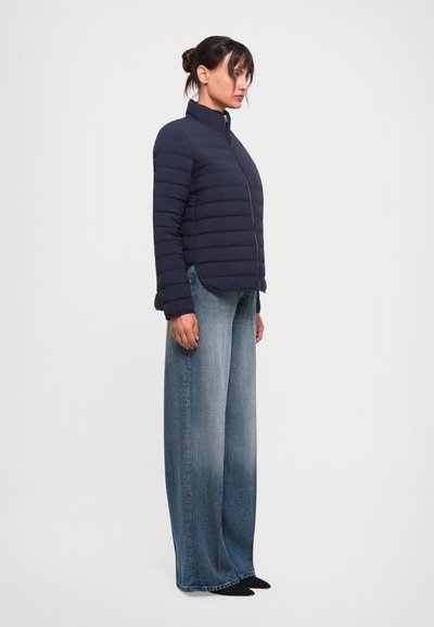 Navy puffer jacket with vertical stitching and high collar, paired with wide-leg light blue denim jeans and black shoes, viewed from the side.