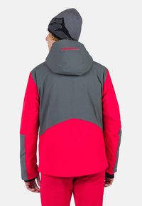 Rode en grijze skijas met een capuchon, met contrasterende kleuren en textuurstof, ontworpen voor wintersporten en buitenactiviteiten.