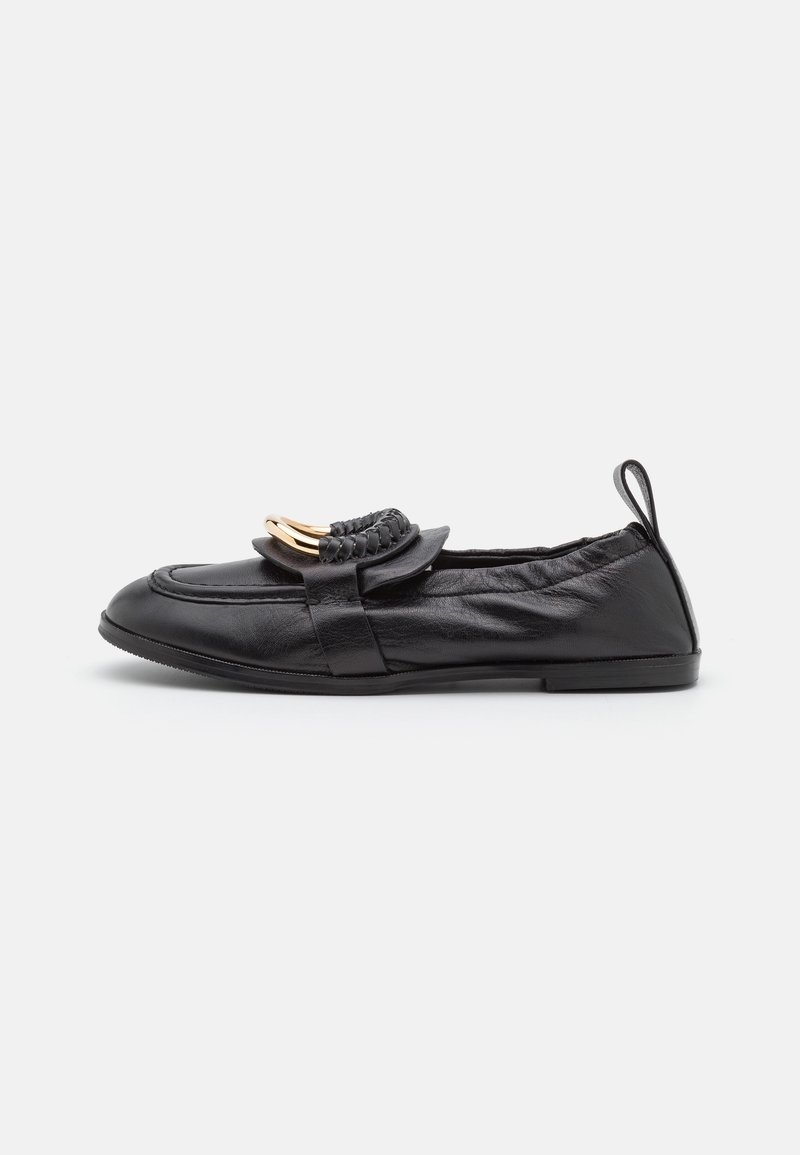 Mocassin plat en cuir noir avec bride tressée et détail métallique doré, bout rond et languette au talon.