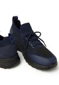Zapatillas deportivas en color azul marino con textura de malla, que presentan una parte superior de punto, acentos en negro y una suela de goma texturizada. Incluyen cordones y una lengüeta.