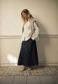 White button-up shirt with rolled sleeves, grey sweater draped over shoulders, dark denim maxi skirt with contrast stitching, light grey peep-toe shoes.