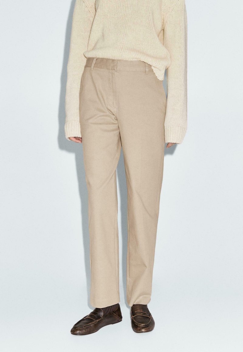 Beige, op maat gemaakte broeken met een rechte pijp, gemaakt van lichtgewicht stof; gecombineerd met donkergrote loafers.