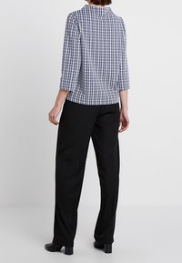 Rutig blus i marinblått och vitt med hög hals, 3/4-ärmar, tillsammans med svarta byxor som visar en lös passform och ett lent tyg.