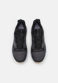 Pár černých a šedých běžeckých tenisek ze síťoviny se šňůrkami, pohled zeshora na bílém pozadí.