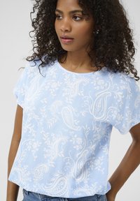 Light blue short-sleeve blouse featuring a white paisley and floral pattern. Soft fabric with a round neckline and relaxed fit.