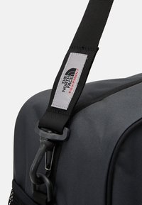 Black fabric duffel bag with a sturdy strap featuring a clip. Includes a gray label with "The North Face" logo and red accents.