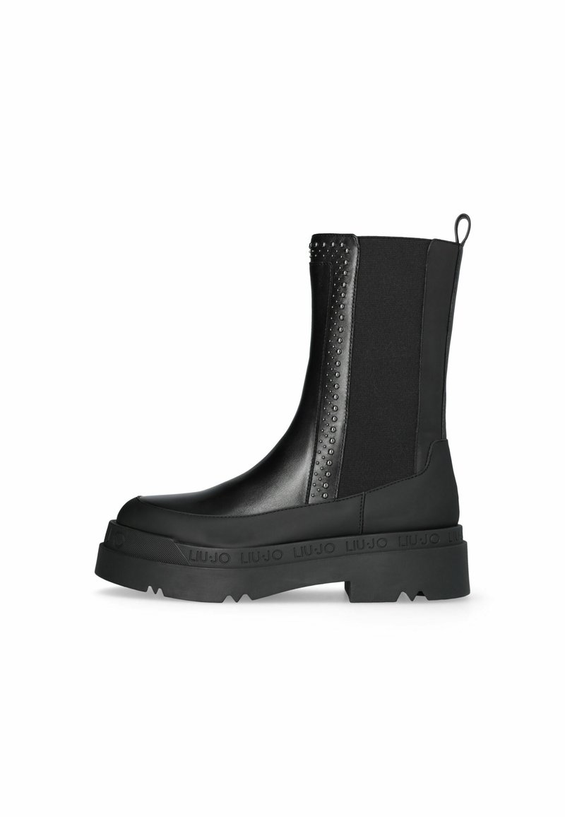 Bottines noires avec une semelle épaisse, fabriquées en matière synthétique lisse. Elles sont dotées de panneaux latéraux élastiques et d'accents cloutés pour le détail.