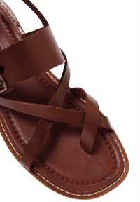 Sandale en cuir marron avec des brides croisées et une semelle plate. Texture lisse et couture blanche contrastante le long du bord. Design classique.