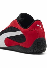 Zapatilla deportiva roja y negra con parte superior texturizada, collar acolchado y suela de goma con un patrón en zigzag. Acento del logo de Puma en blanco.