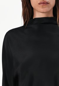 Black satin top with a high neck, smooth texture, and minimalist design. Features a relaxed fit and subtle sheen.