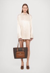 Chemise argentée satinée de couleur beige clair avec un col ; sac fourre-tout en brun à motifs avec un logo doré et des accents en cuir brun ; mocassins bruns.