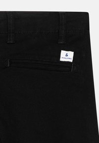Gros plan sur la poche arrière d'un pantalon noir avec passants de ceinture et une étiquette blanche indiquant "Jack & Jones" en texte bleu.
