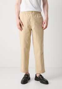 Beige bomullsbukser med elastisk midje og knappelukking. Rett ben-design, med sidelommer og glatt tekstur.