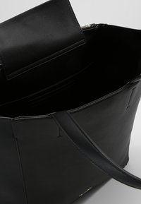 Czarna skórzana torba tote o gładkiej fakturze, otwartym górnym wejściu, pojedynczym uchwycie oraz wewnętrznych kieszonkach na karty. Minimalistyczny design bez widocznych dodatków.