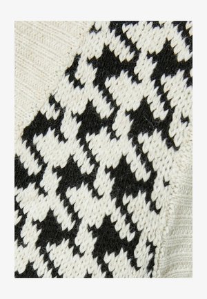 Neulepusero, jossa on musta ja kerma houndstooth-kuviointi, yhdistettynä teksturoituun kankaaseen ja sileisiin, yksivärisiin osiin.