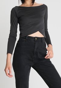 Top corto nero a maniche lunghe con scollo a barca e design frontale torto, abbinato a jeans in denim neri a vita alta.