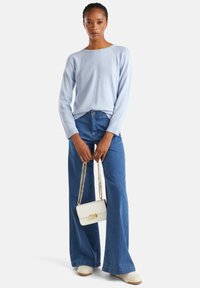 Pull en tricot bleu clair à manches longues, associé à un jean flare en denim taille haute. Portant un sac à main blanc avec une bandoulière en chaîne dorée.