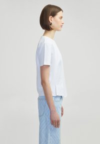 Blusa blanca de manga corta, hecha de una tela suave, con un escote redondo y pliegues laterales, combinada con jeans de patrón en zigzag de color azul claro.