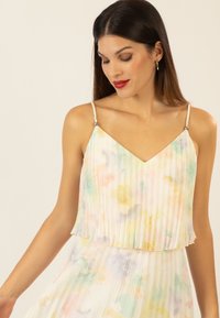 Top camicia in tessuto plissettato con motivo floreale in colori pastello, spalline regolabili e dettagli in metallo argentato, caratterizzato da un design a strati e una texture trasparente.
