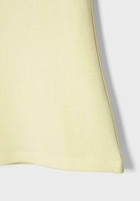 Angolo di tessuto giallo morbido con cuciture visibili e una leggera piega sul lato destro su uno sfondo grigio chiaro.