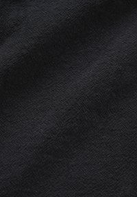 Gros plan sur un tissu foncé à texture avec un motif de tissage subtil en forme de grille et des plis doux créant des ombres.