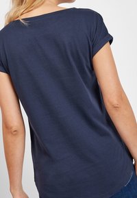 Camiseta de manga corta de color azul marino con un corte relajado. Cuello redondo y puños enrollados. Tejido suave con una textura lisa. Diseño básico, sin estampados.