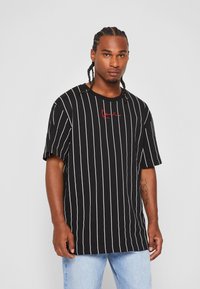 T-shirt à rayures noires et blanches avec une coupe décontractée, manches courtes et logo rouge brodé. Matière en coton, design à col rond.