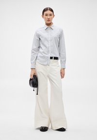 Cămașă cu dungi, cu nasturi, în albastru deschis și alb, asortată cu pantaloni largi crem. Accesoriu: geantă mică neagră cu șnur.