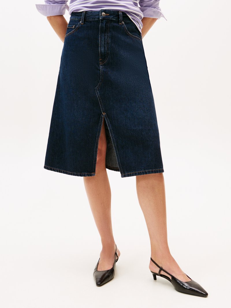 Donkerblauwe denim midi-rok met een split aan de voorkant, vijf zakken en contrasterende stiksels. Gecombineerd met zwarte slingback-schoenen met puntige neuzen.