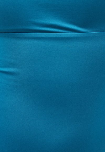 Κοντινό πλάνο λείας μπλε υφασμάτινης επιφάνειας με οριζόντια ραφή κοντά στο πάνω μέρος και ελαφριές ρυτίδες που δημιουργούν μαλακές πτυχώσεις.