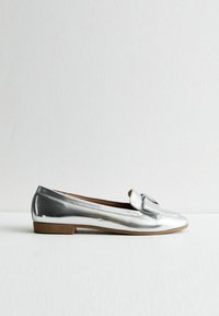 Srebrne metaliczne loafersy na płaskim obcasie, z akcentem w postaci kokardki na cholewce. Gładka tekstura i smukły design z zaokrąglonym noskiem.