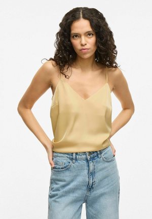 Satin camisole in light yellow with a V-neck and thin straps, paired with high-waisted light blue jeans, featuring distressed detailing.