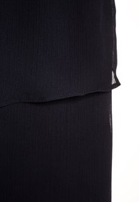 Tissu plissé bleu marine foncé avec un design à couches et une texture de fines nervures verticales sur un fond blanc.