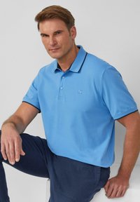 Light blue polo shirt with a flat collar and two-button placket, featuring a contrasting navy trim and embroidered logo on the left chest.