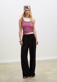 Dopasowany różowy top na ramiączkach z prążkowanej tkaniny nałożony na biały t-shirt, w połączeniu z szerokimi czarnymi spodniami. Modelka nosi również chustę w kwiatowy wzór.