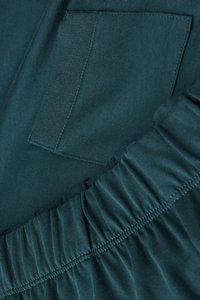 Tyrkysová tkanina s texturovanou panelem a rýhovaným lemem. Obsahuje malou náprsní kapsu na levé straně, která zvyšuje design.