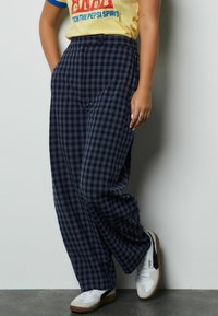 Marineblauwe en grijze geruite wijde broek met een nauwsluitende pasvorm, voorzien van een knoopsluiting en zijzakken, gecombineerd met witte sneakers.