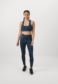 Set di reggiseno sportivo e leggings in teal scuro con motivi astratti; texture liscia; progettato per l'abbigliamento attivo; abbinato a scarpe da ginnastica nere.