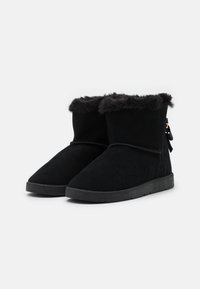 Stivali alla caviglia in suede nero con finiture in pelliccia sintetica nella parte superiore, suola piatta in gomma e dettaglio a fiocco decorativo sul retro.