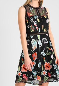 Czarna haftowana sukienka z dopasowanym gorsetem i rozkloszowanym dołem, ozdobiona kolorowymi kwiecistymi wzorami oraz teksturowaną siateczką na wierzchu.