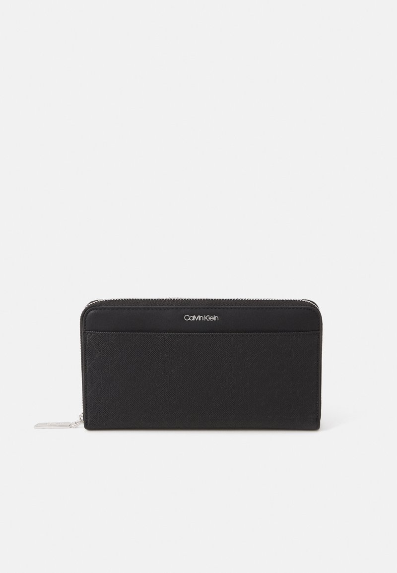 Black zip-around wallet made of textured fabric, featuring a logo patch and a flat pocket. Rectangular shape with smooth edges.