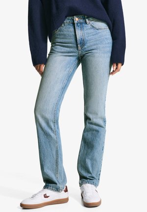 Light blue jeans with a straight-leg cut, made from denim. Features classic five-pocket design and subtle fading. Paired with white sneakers.