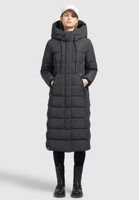 Cappotto imbottito nero con cappuccio, caratterizzato da un design trapuntato, due tasche anteriori con zip e una lunghezza fino al ginocchio, abbinato a stivali neri al ginocchio.