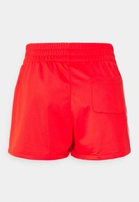 Červené sportovní šortky s elastickým pasem, hladkou texturou a jedním zadním kapsou. Mají čistý, minimalistický design.