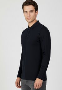 Granatowa koszulka polo z długim rękawem, wykonana z gładkiej tkaniny, z zapięciem na guziki i subtelnym logo na piersi.