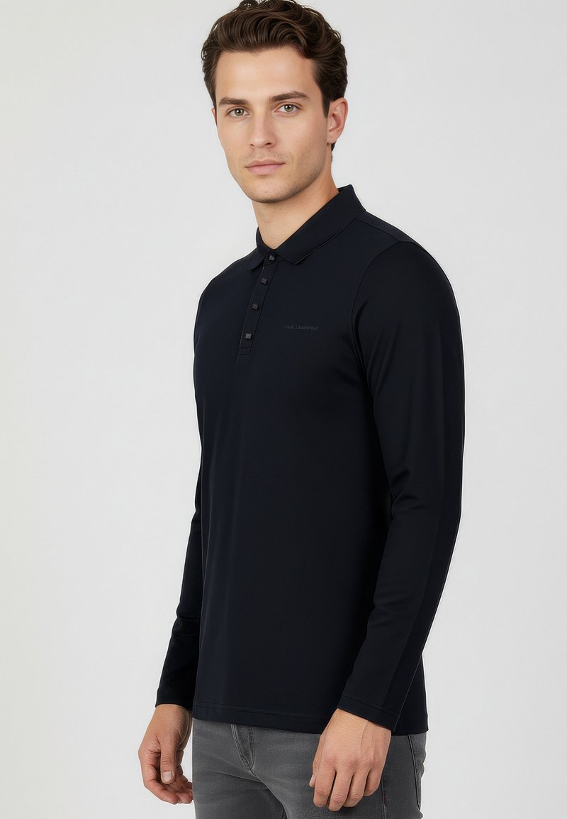 Granatowa koszulka polo z długim rękawem, wykonana z gładkiej tkaniny, z zapięciem na guziki i subtelnym logo na piersi.