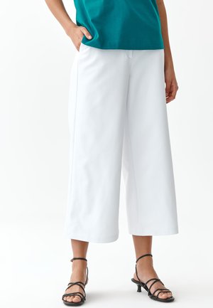 Pantaloni bianchi a gamba larga con una texture liscia, caratterizzati da una vita alta e tasche laterali. Abbinati a tacchi neri con cinturini per creare un contrasto.