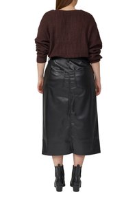 Bruine gebreide trui, zwarte leren midirok met achterzakken, slim fit, zichtbare naden, gecombineerd met zwarte enkellaarsjes.